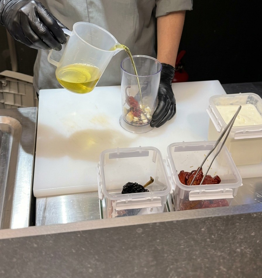 Lo chef versa un liquido trasparente in un bicchiere da frullatore alto contenente aglio e peperoncini.