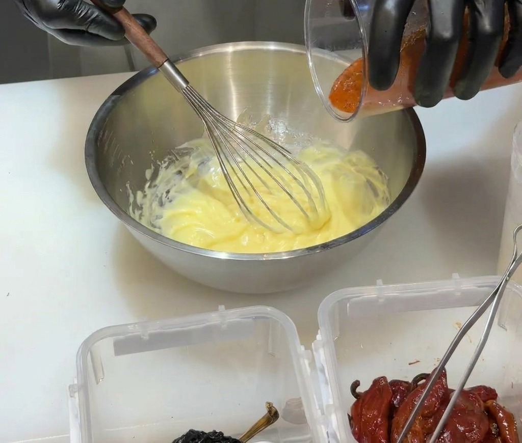 Versare la purea di peperoncino rosso frullato in una base di maionese gialla in una ciotola di metallo.