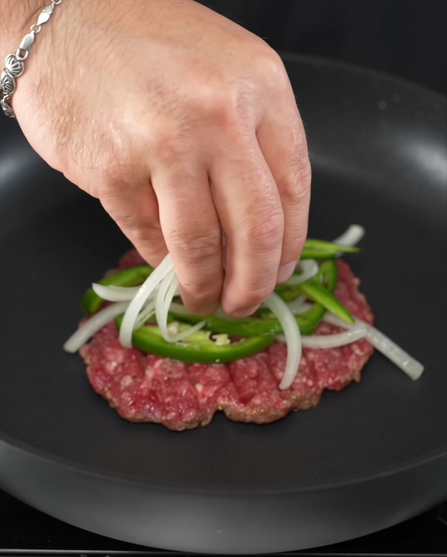 Anelli di jalapeño fresco e fette di cipolla posizionati sopra un medaglione di manzo sfrigolante.