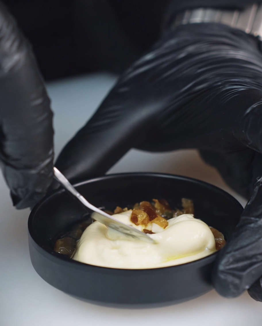 Primo piano di una ciotolina contenente maionese, peperoncini messicani tritati e succo di cetriolini mentre vengono mescolati con un cucchiaio di metallo.
