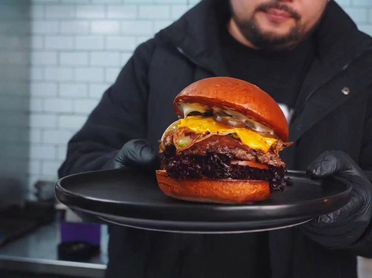 Un hamburger scottato sulla piastra guarnito con le verdure saltate e una fetta di formaggio che si scioglie.