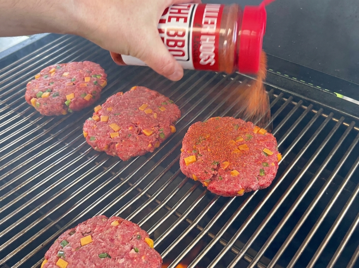Hamburger di manzo conditi con rub per BBQ adagiati sulla griglia.