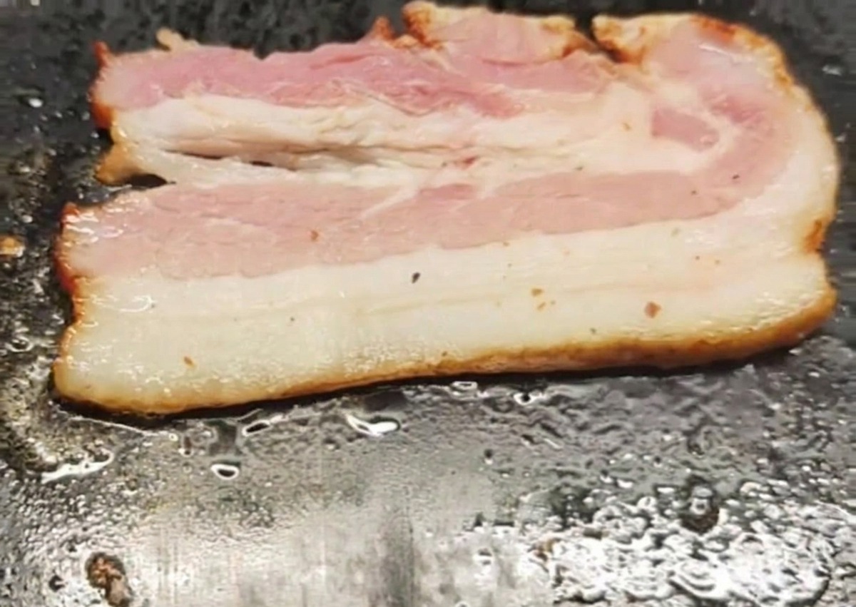 Una striscia di bacon che frigge su una piastra calda.