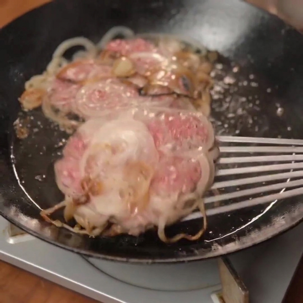 Un disco di smash burger appena cotto con formaggio fuso posizionato su un panino tostato.