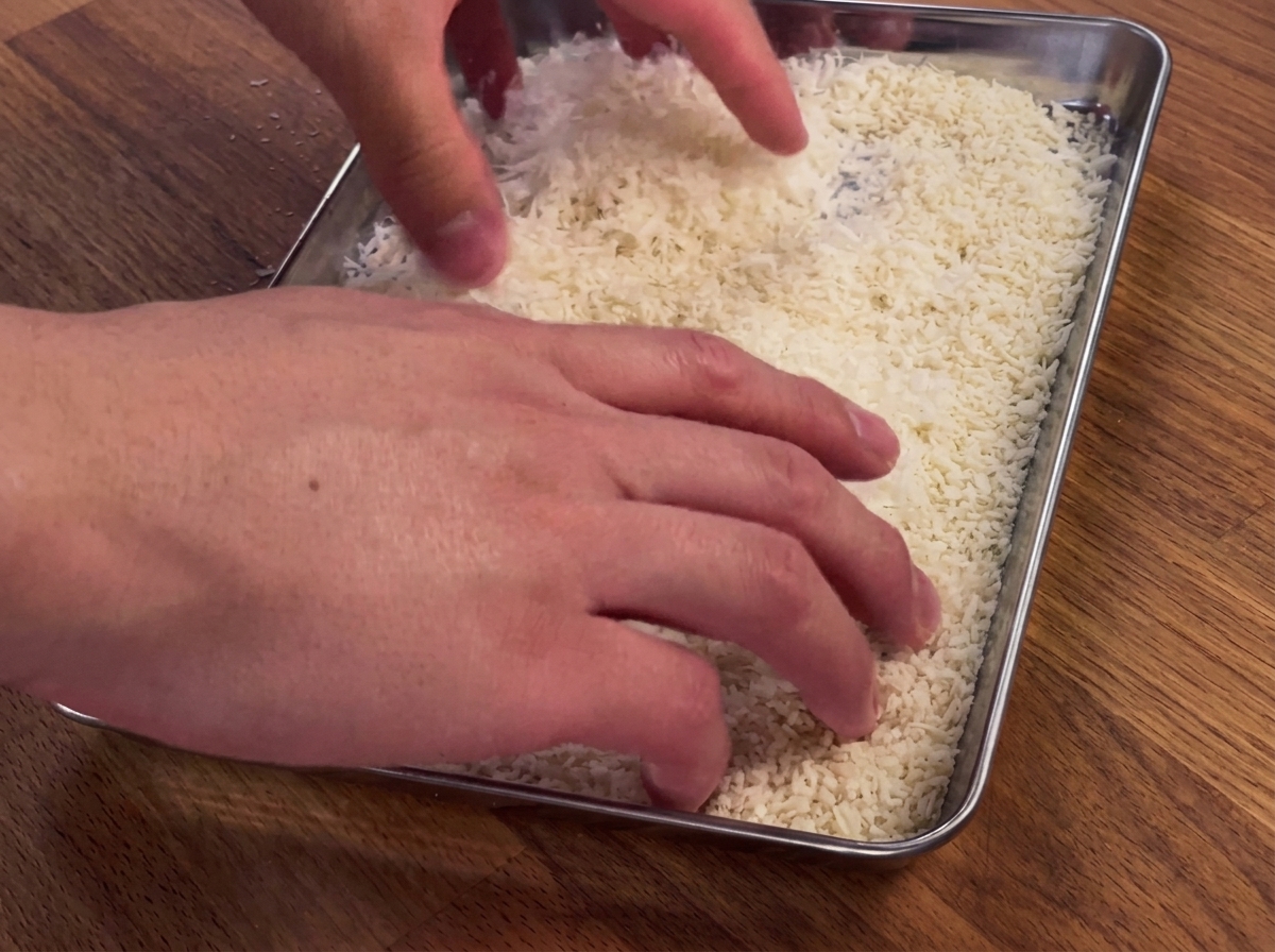 Mani che premono un petto di pollo in una teglia di pangrattato e parmigiano.