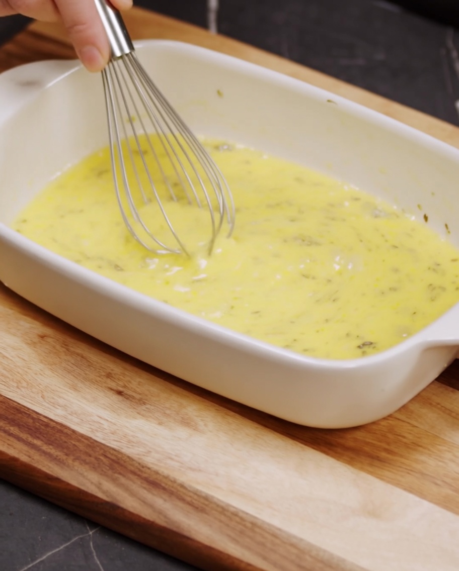 Una frusta che mescola pangrattato, parmigiano grattugiato e pepe nero in una teglia di ceramica bianca.