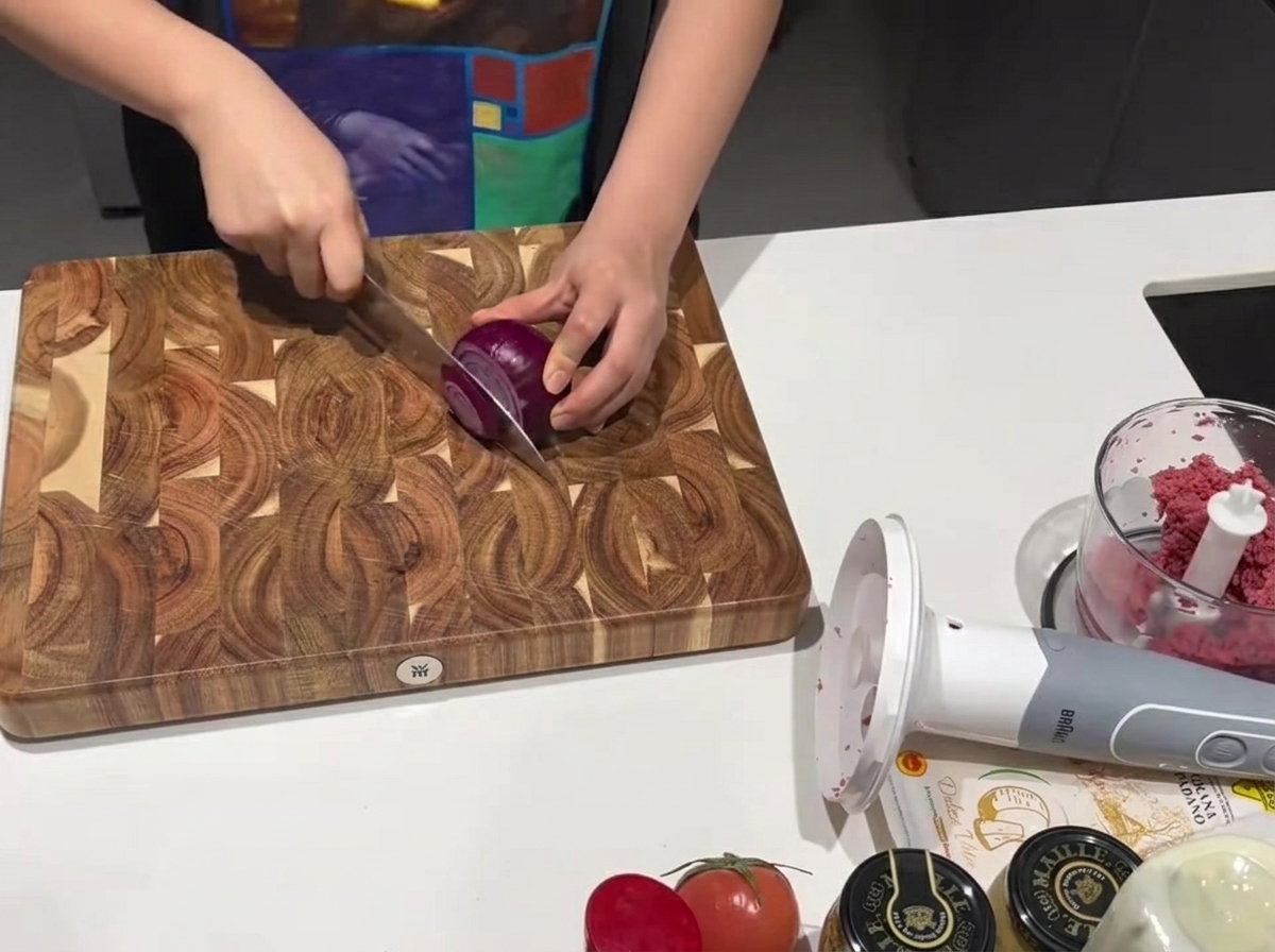 Un coltello affilato taglia una cipolla rossa fresca su un tagliere di legno.