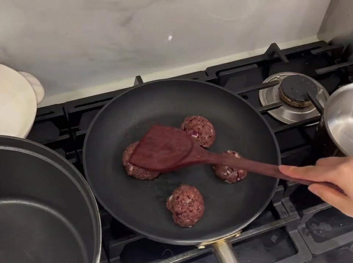 Polpette di carne pressate in una padella calda con una spatola di metallo.
