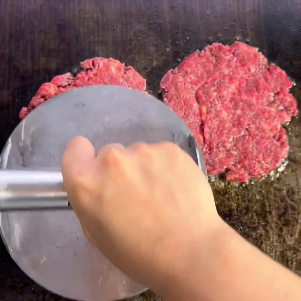 Due hamburger di manzo sfrigolanti sulla griglia con una crosticina ben rosolata.