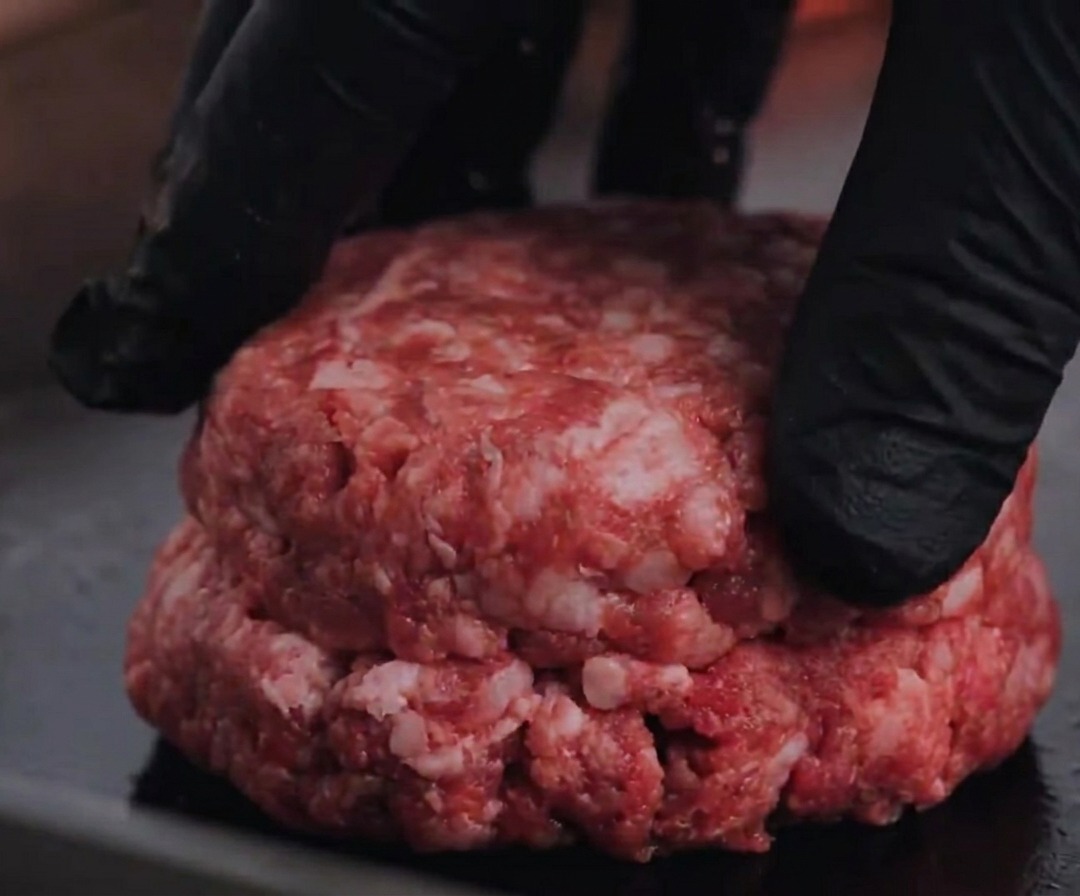 Un hamburger di carne Angus pressato su una piastra calda.