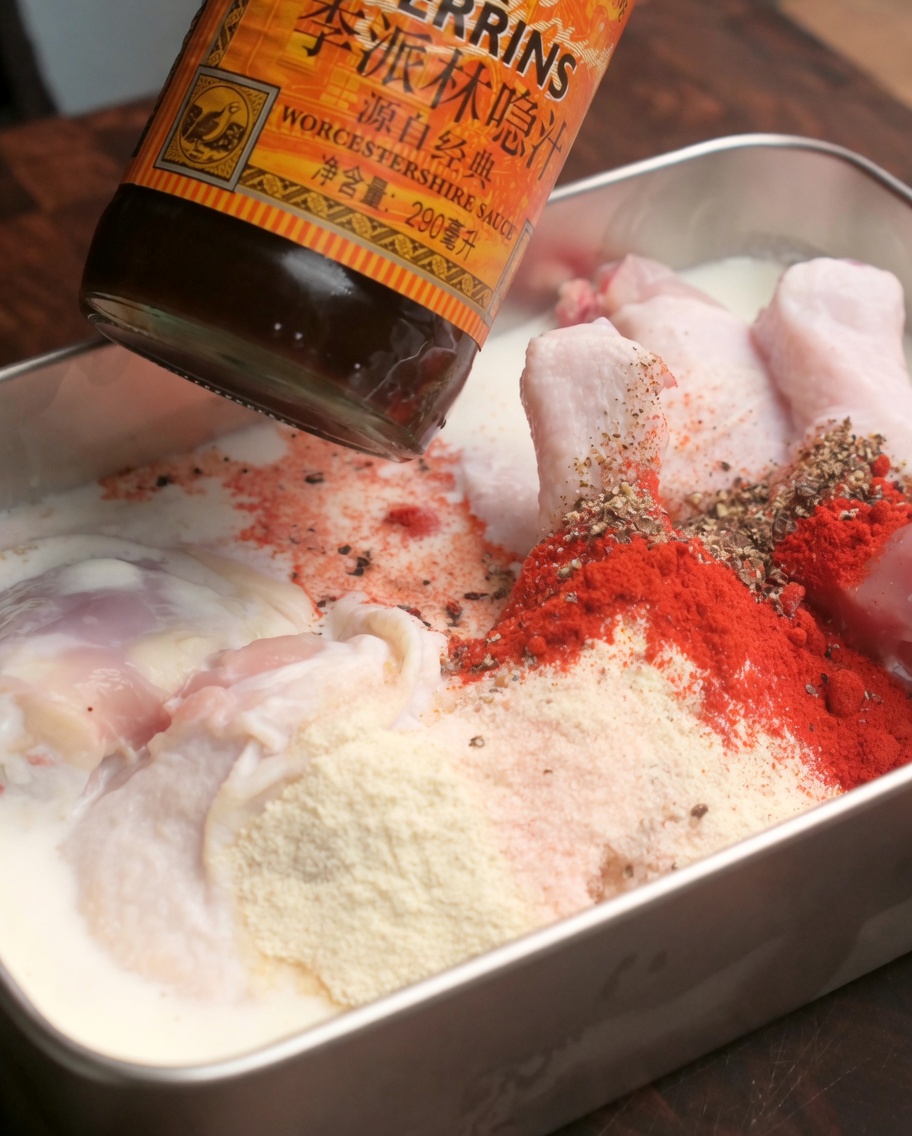 Salsa Worcestershire gocciolata in un vassoio di cosce di pollo crude marinate e ricoperte di spezie rosse in polvere.