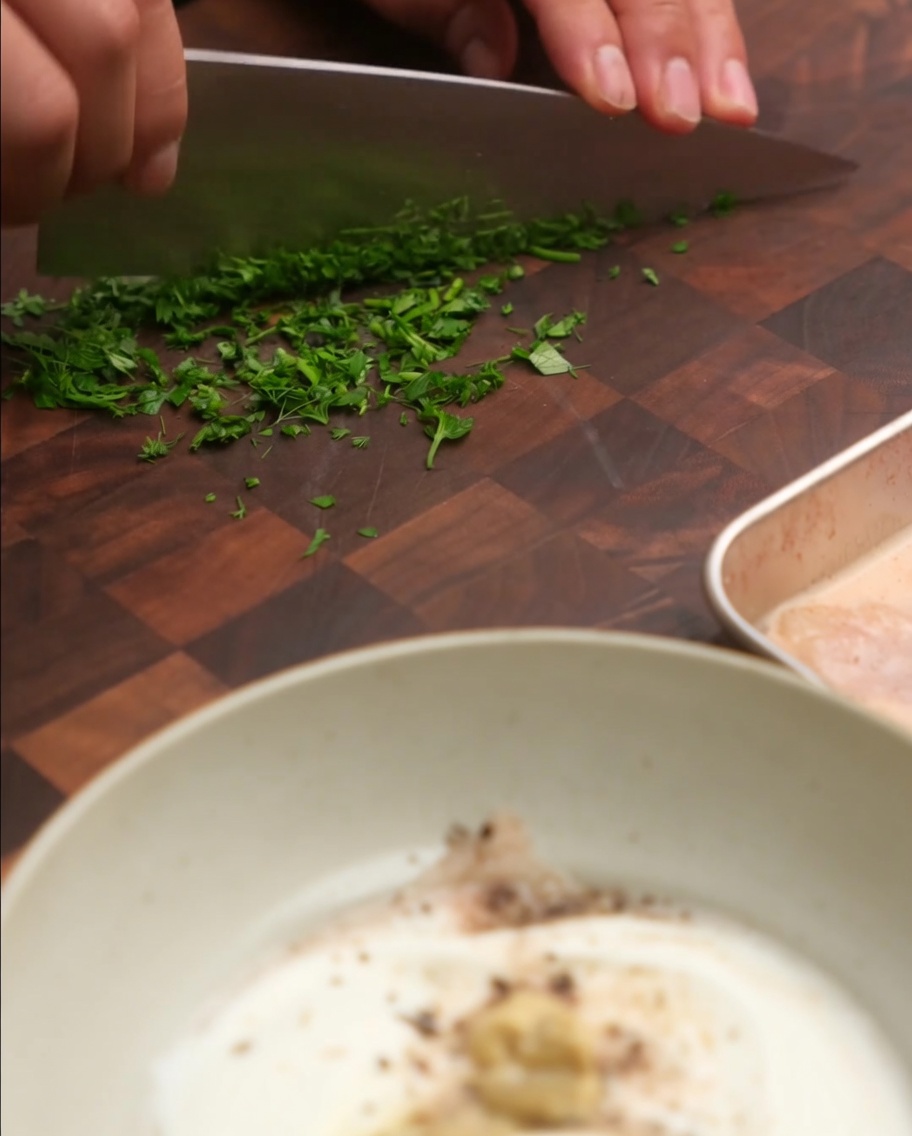 Erba cipollina fresca e prezzemolo tritati aggiunti in una ciotola con yogurt e altri ingredienti per la salsa.