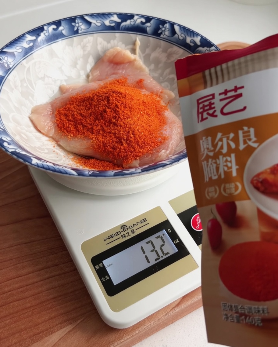 Polvere per marinatura Orleans pesata in una ciotola contenente un petto di pollo crudo.