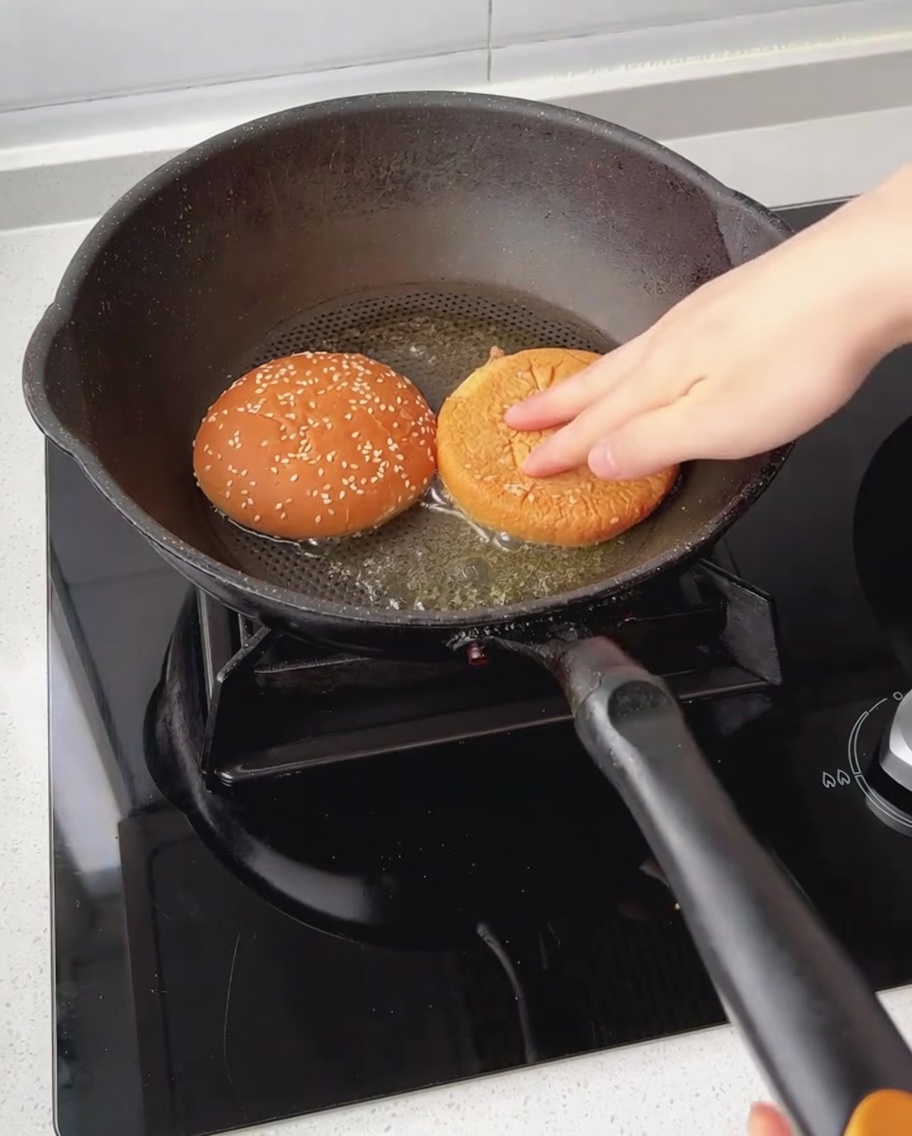 Metà del panino da hamburger tostate a faccia in giù in una padella con burro fuso.