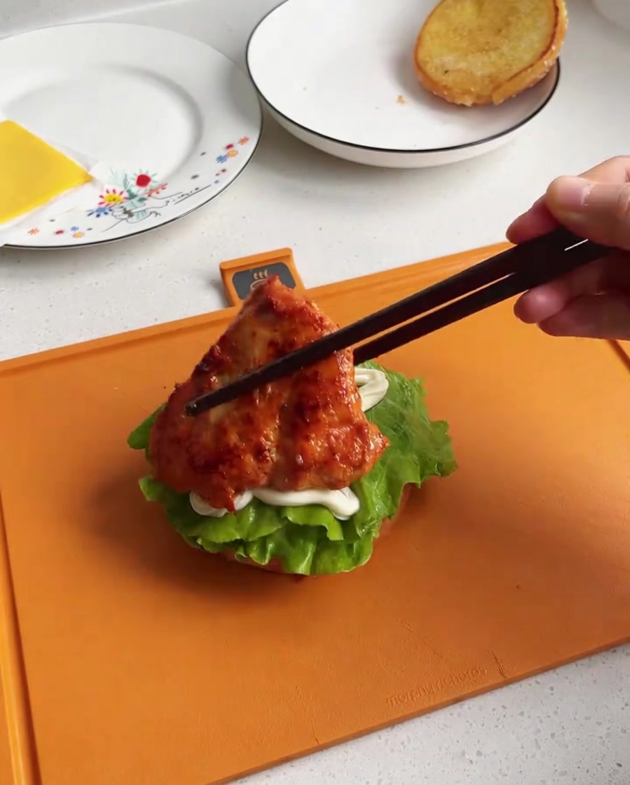 Un pezzo di pollo cotto e glassato posizionato su una base di pane con lattuga e maionese.