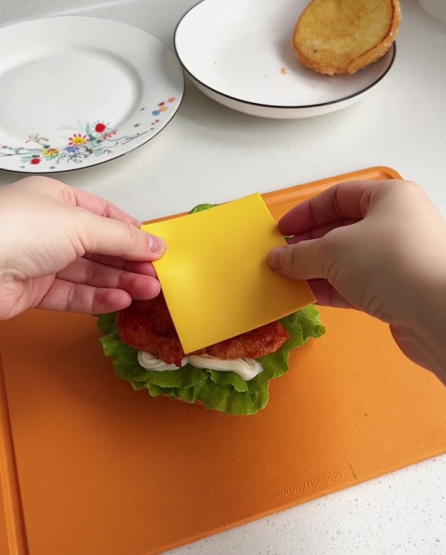 Una fetta di formaggio giallo centrata sopra il pezzo di pollo caldo sulla base dellhamburger.