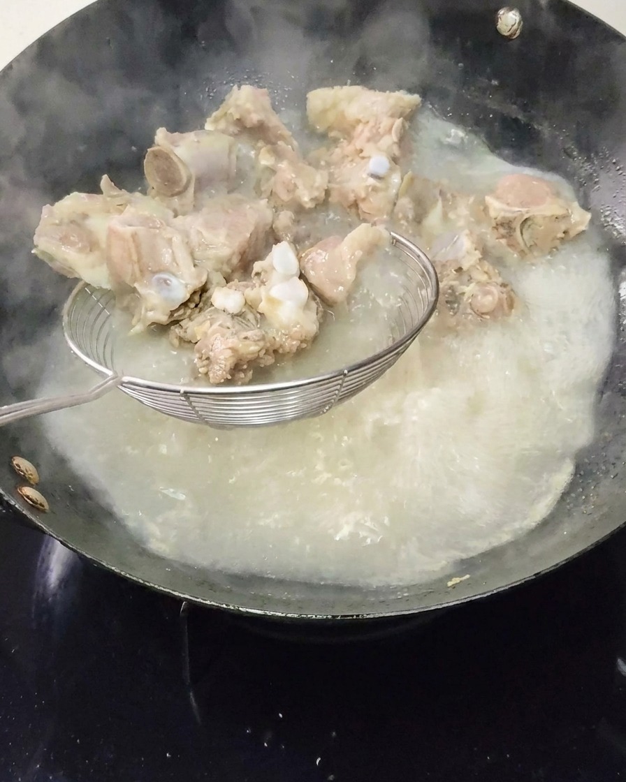 Costolette di maiale sbollentate estratte dallacqua bollente con una schiumarola.