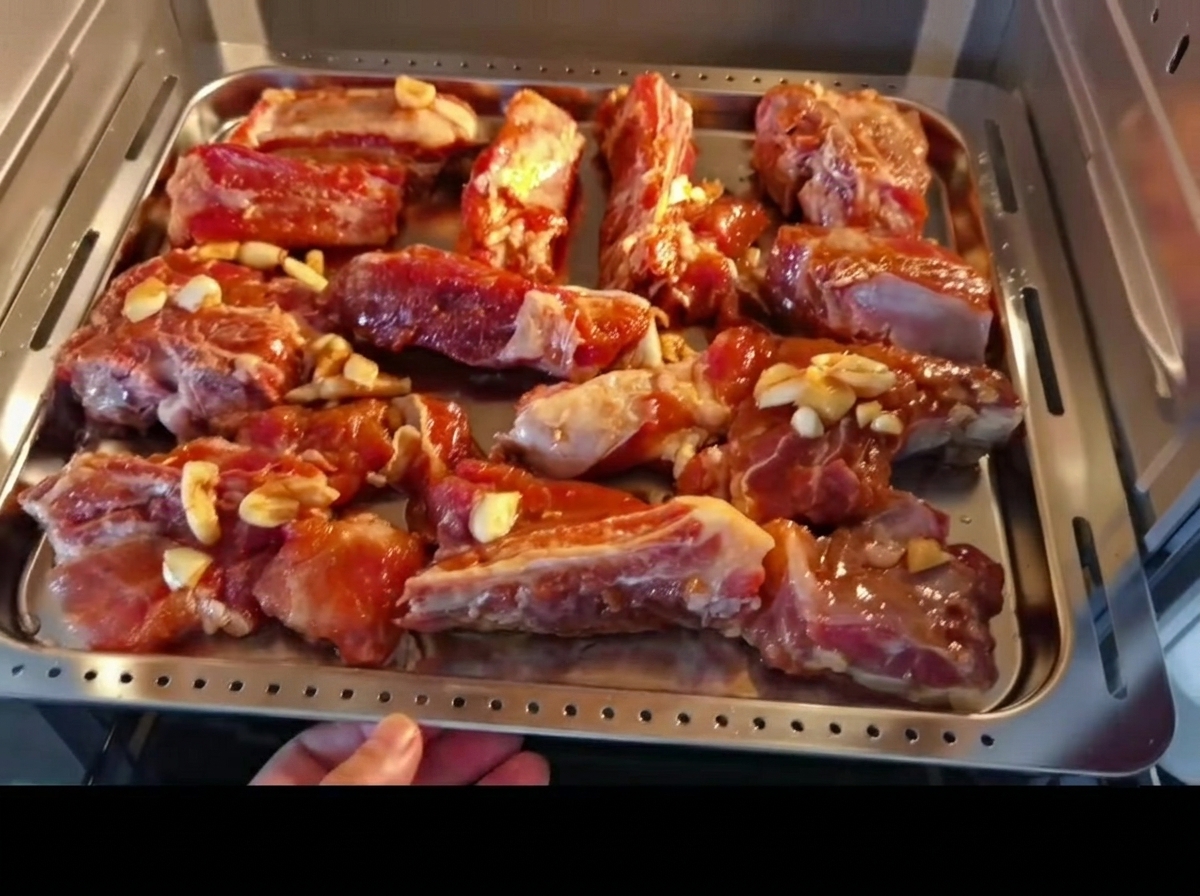 Costine di maiale marinate disposte uniformemente su una teglia da forno, mentre vengono inserite nel forno.