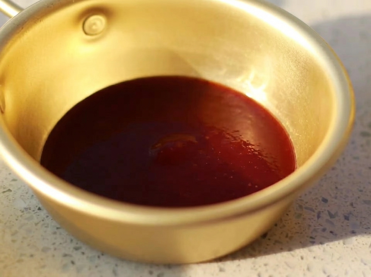 Una piccola ciotola di metallo contenente una miscela liscia di salsa barbecue, salsa di ostriche, senape, miele e salsa di soia chiara.