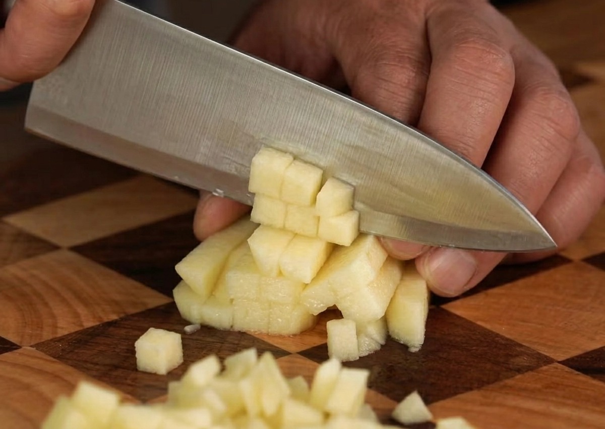 Una mela fresca tagliata a cubetti piccoli e uniformi su un tagliere di legno.