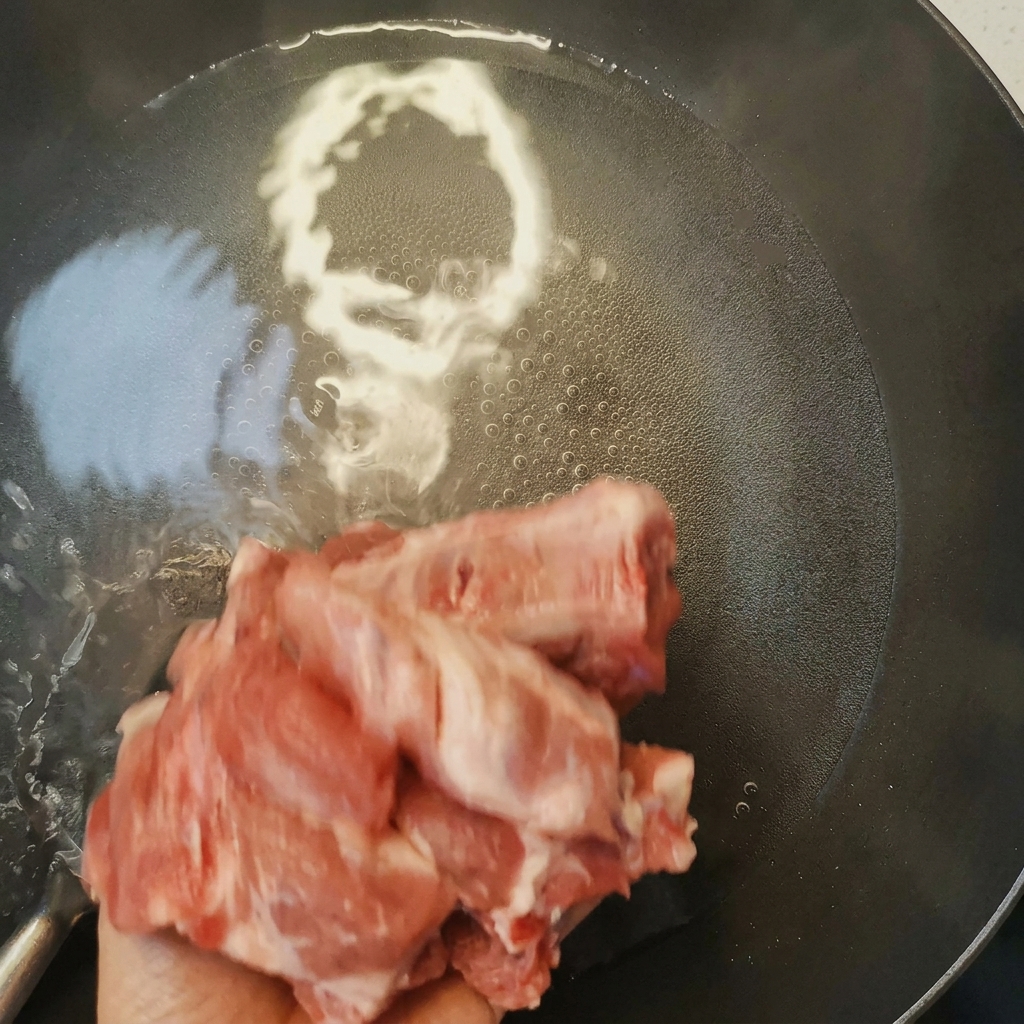 Costine di maiale che sbollentano in una pentola con acqua bollente e vino da cucina, con schiuma in superficie.