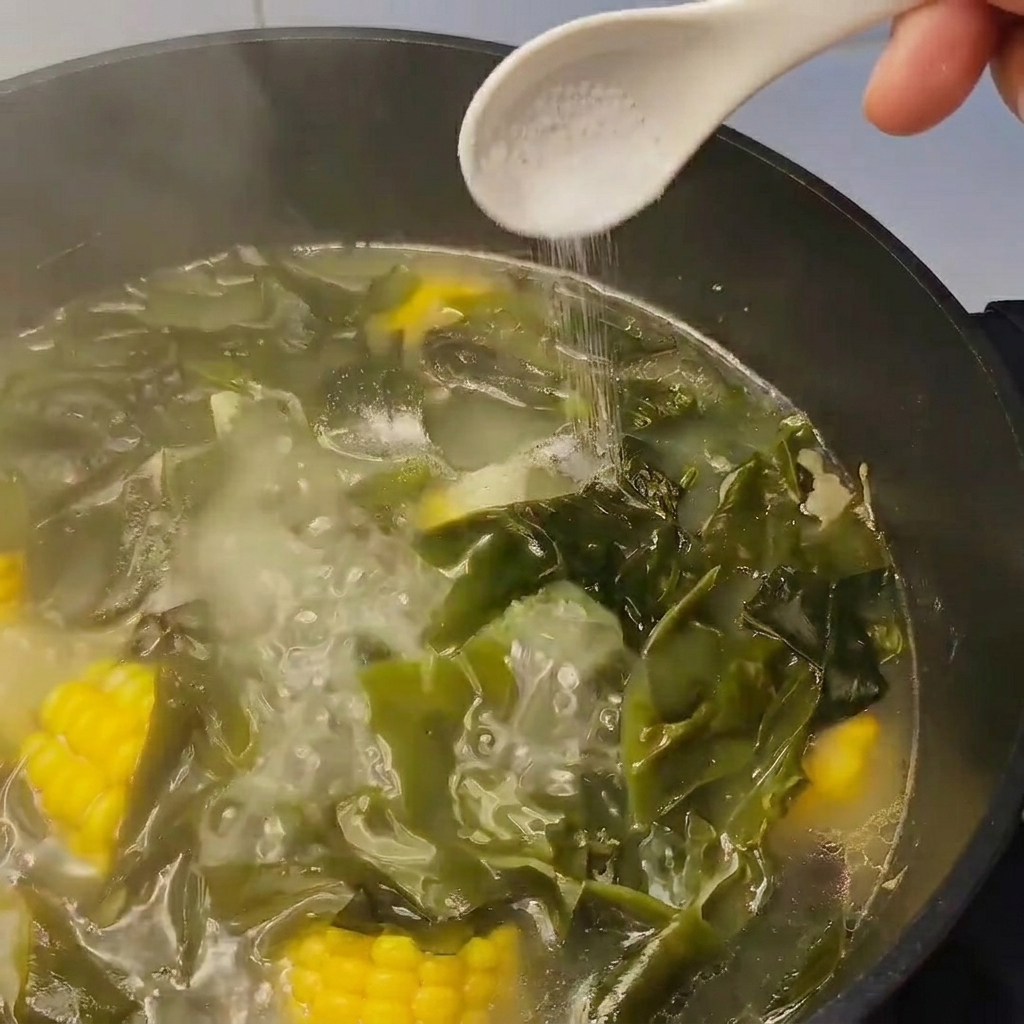Un cucchiaio di sale aggiunto a una pentola di zuppa con alghe e mais.