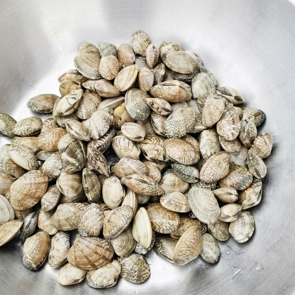 Vongole fresche in una bacinella di metallo mentre vengono sciacquate con acqua pulita.