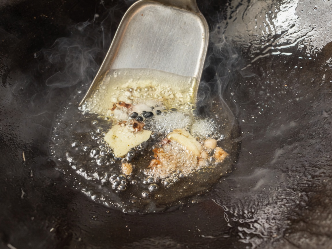 Spezie, zenzero e cipollotti che sfrigolano in olio caldo dentro un wok.