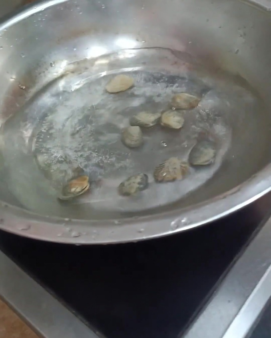 Vongole che cuociono in una pentola di acqua bollente, con alcuni gusci che iniziano ad aprirsi.