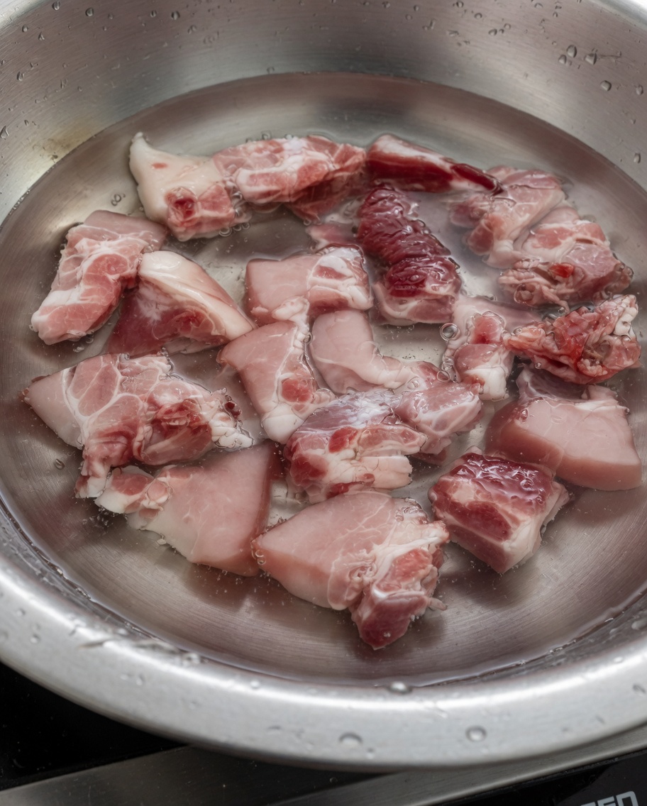 Pezzi di costine di maiale che bollono in acqua per rimuovere le impurità.