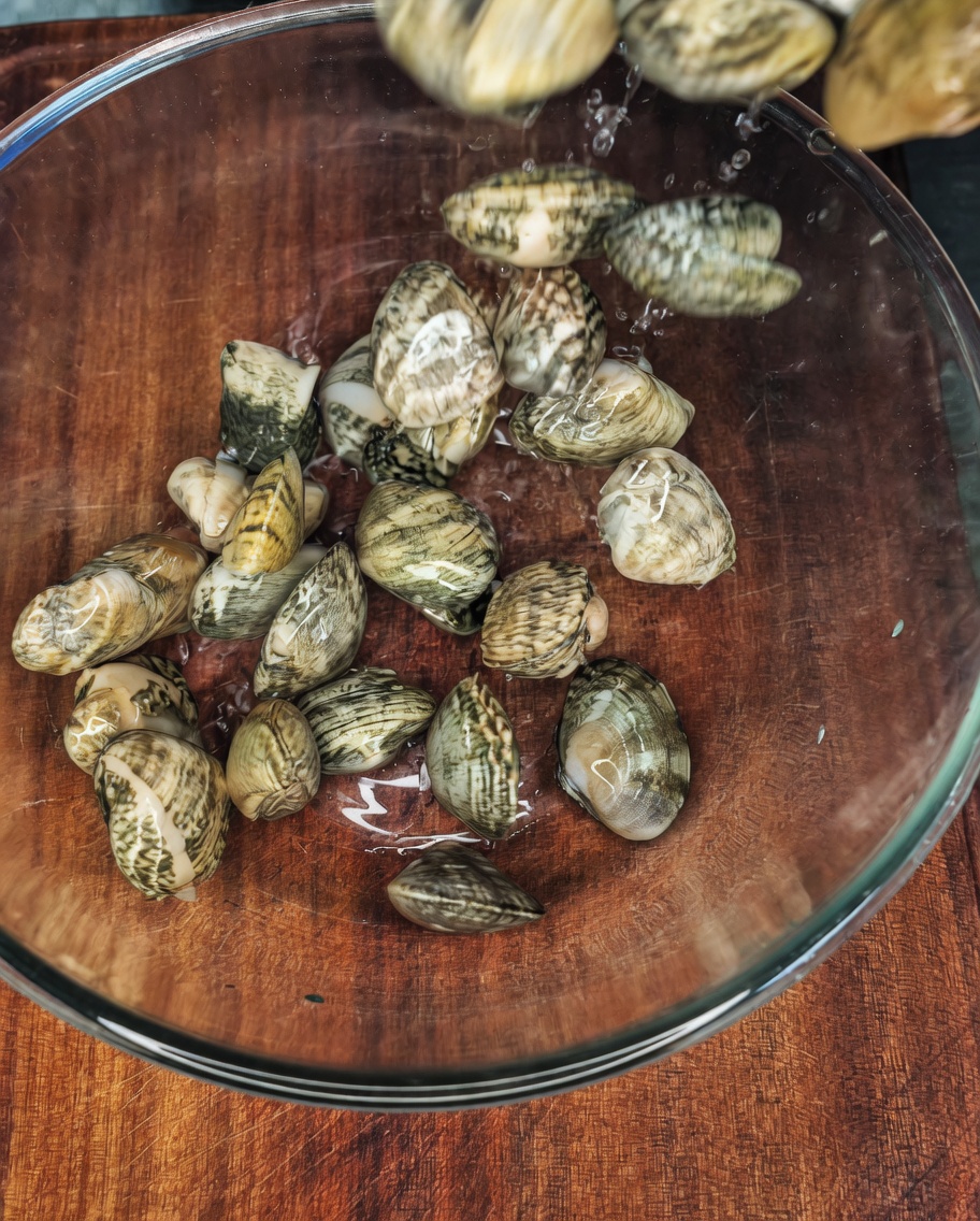 Vongole fresche in una ciotola di vetro trasparente riempita con acqua, sale e un filo dolio.