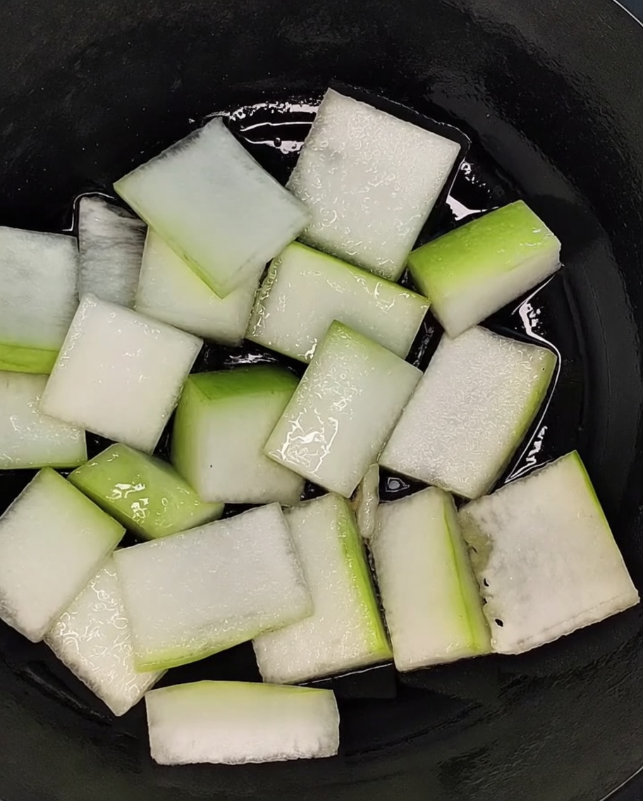 Fette di melone invernale disposte uniformemente a coprire il fondo di una pentola nera.