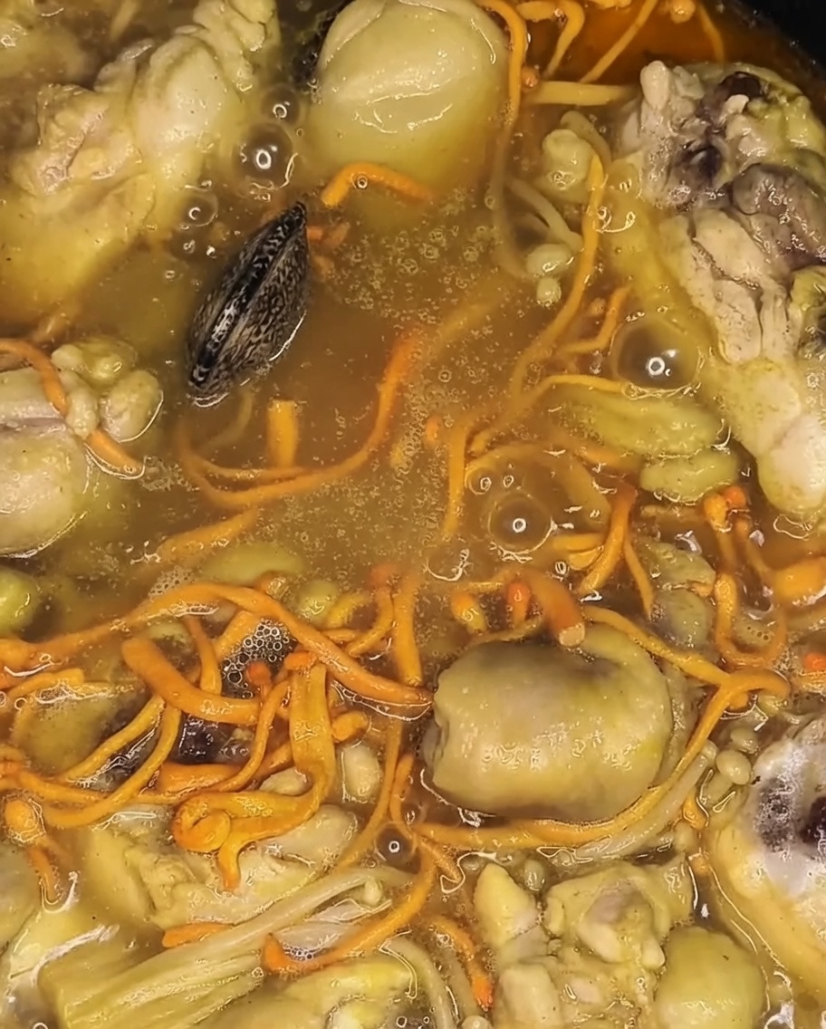 Vongole fresche aggiunte alla pentola in ebollizione, appoggiate sopra il pollo e le verdure cotte.