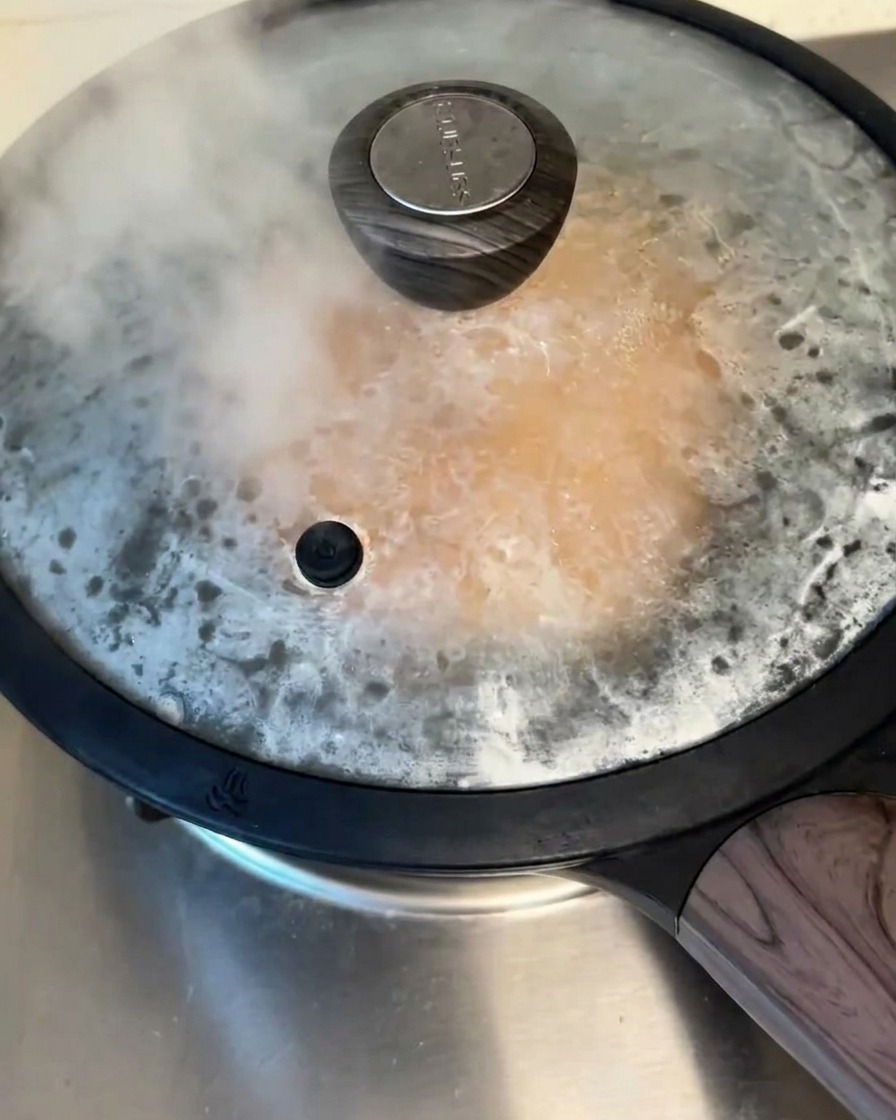 Una padella antiaderente coperta sul fornello, con vapore visibile che fuoriesce sotto il coperchio mentre il pancake cuoce.
