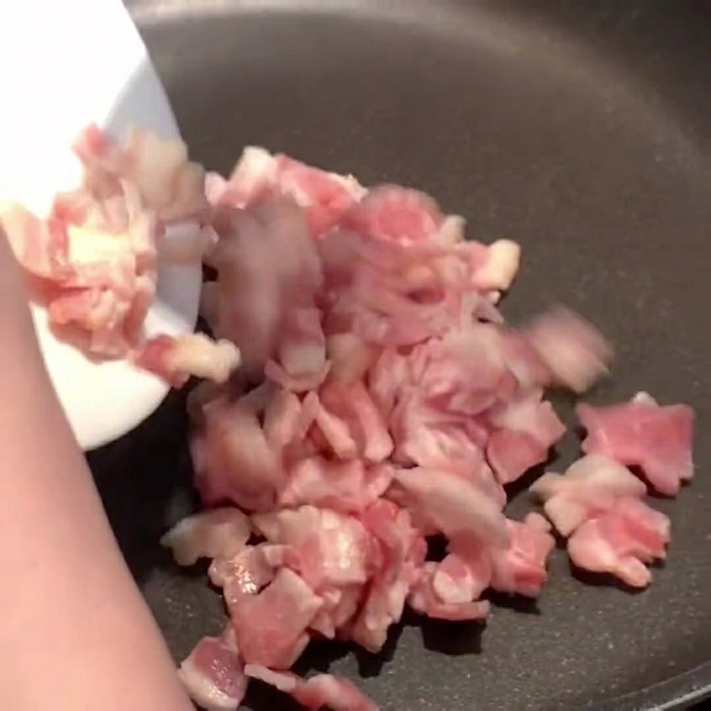 Pezzetti di bacon che sfrigolano in padella rilasciando il grasso dorato.