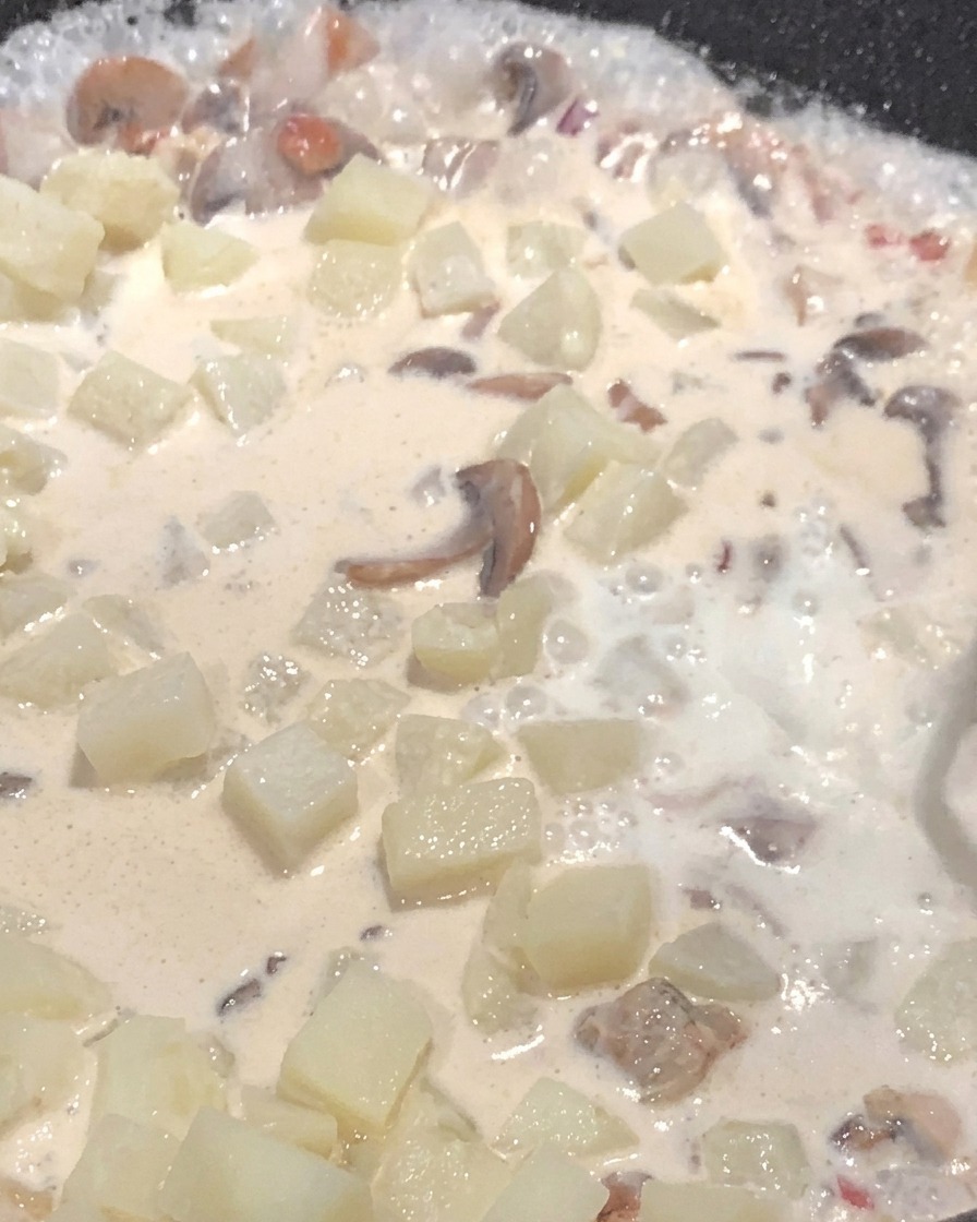 Latte versato nella padella con patate e funghi che sobbollono nella salsa cremosa.