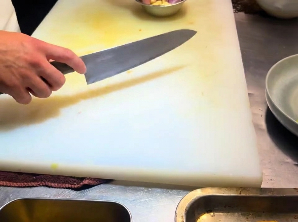 Spicchi daglio affettati sottilmente disposti su un tagliere bianco.