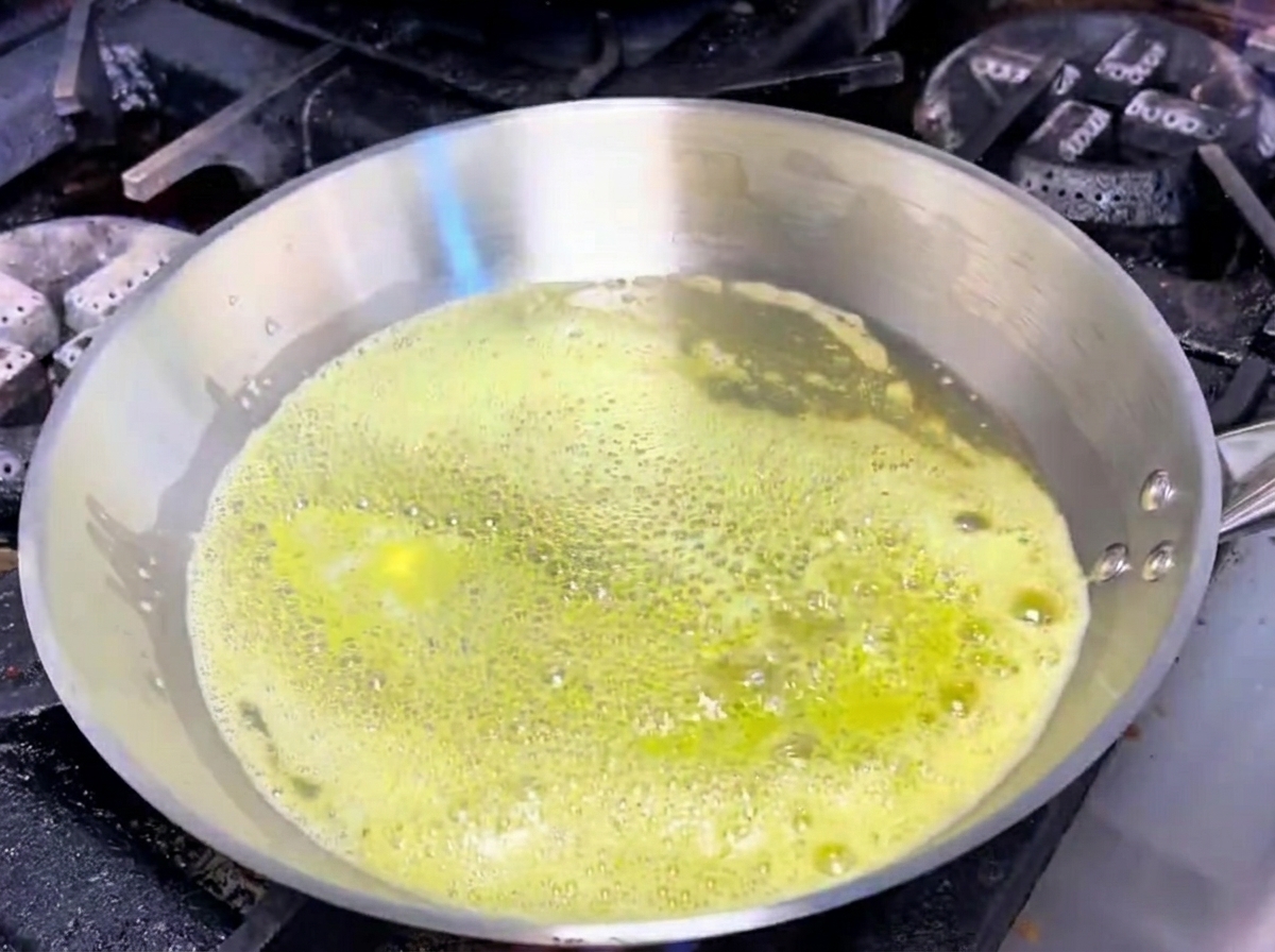 Aglio e scalogni che sfrigolano nel burro fuso allinterno di una padella di acciaio inossidabile.