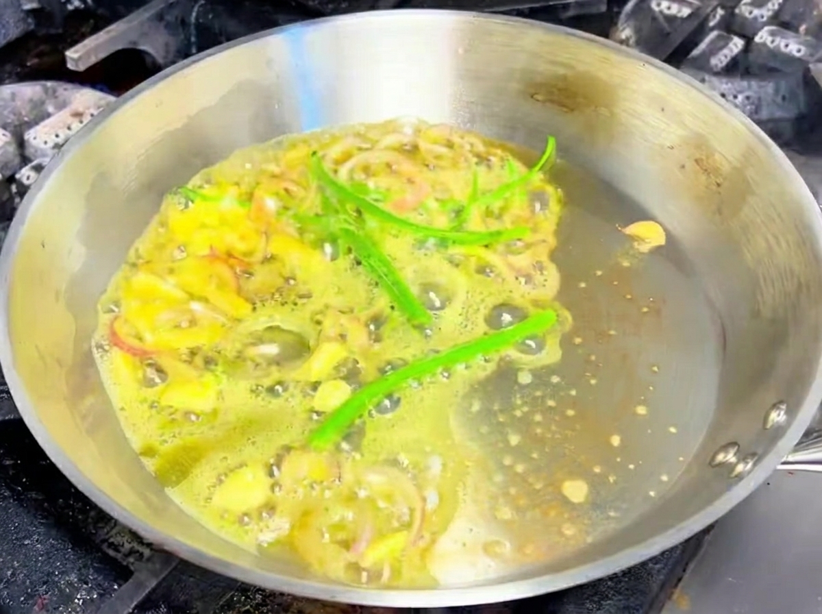 Aglio affettato, scalogni e peperoncini verdi che sfrigolano nel burro fuso in una padella di acciaio inossidabile.