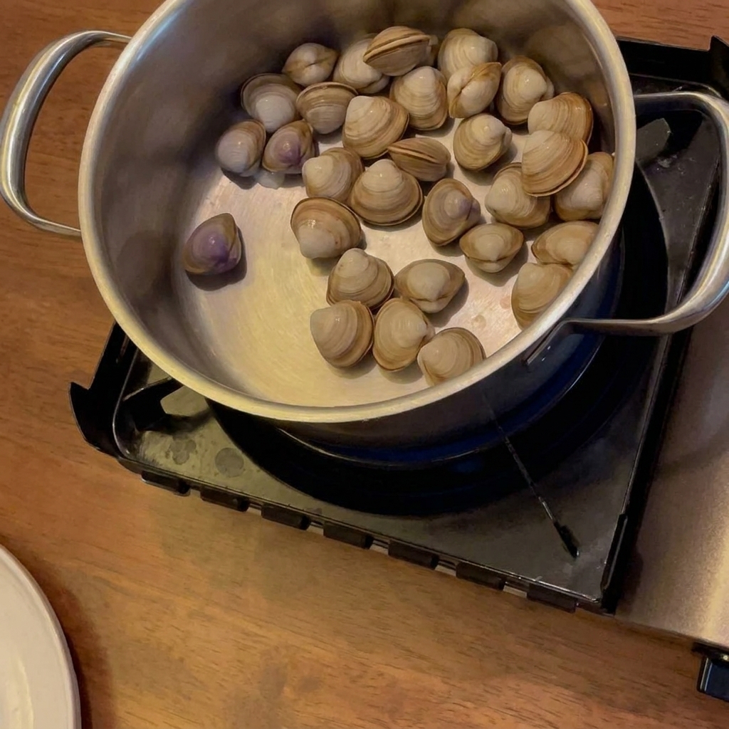 Alcol versato in una pentola con vongole, patate e carote su un fornello portatile.