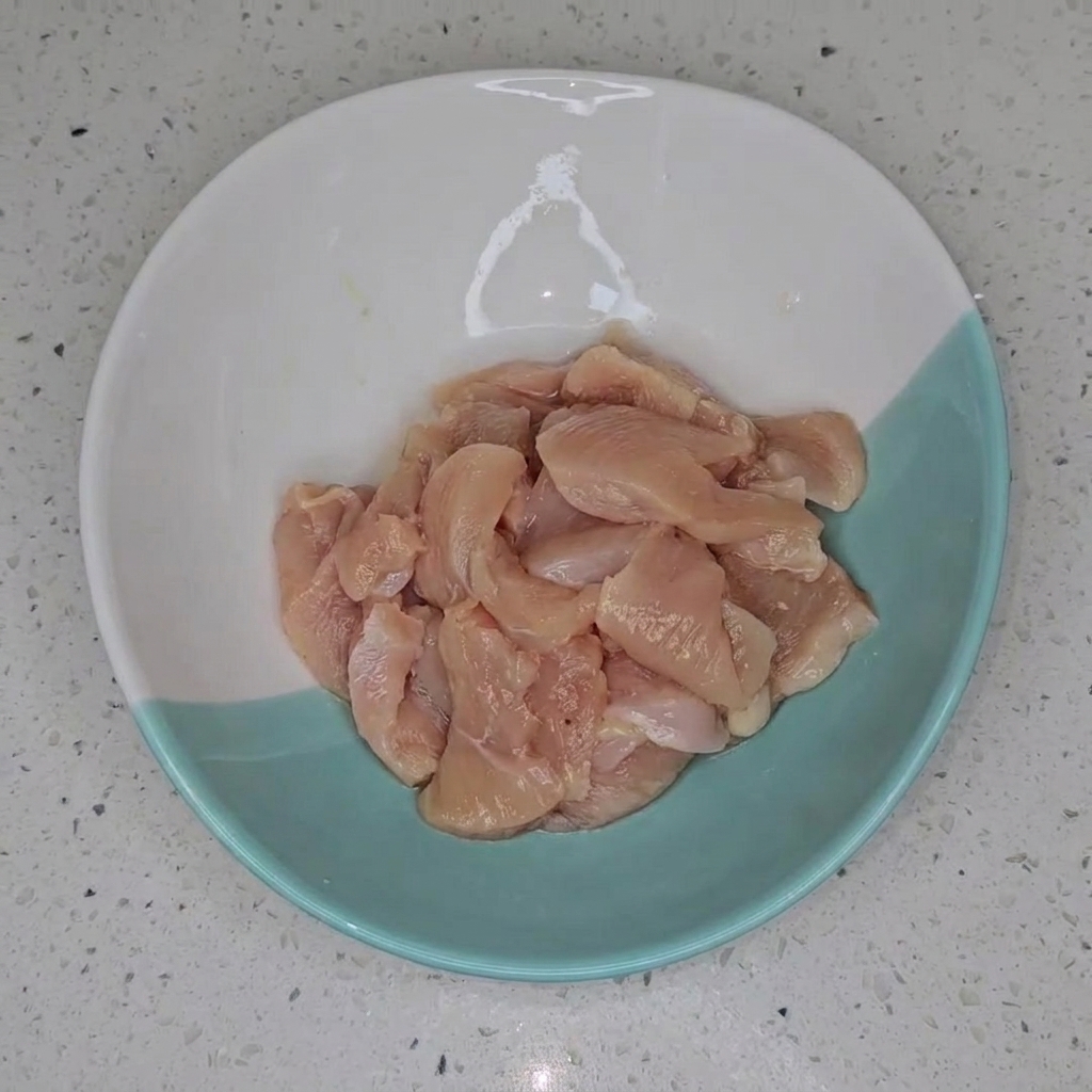 Pezzetti di petto di pollo marinati in una ciotola, pronti per la cottura.