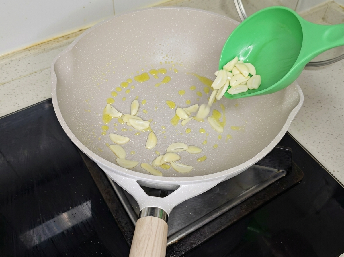 Aglio a fette e cipollotto tritato che sfrigolano in padella con olio doliva.