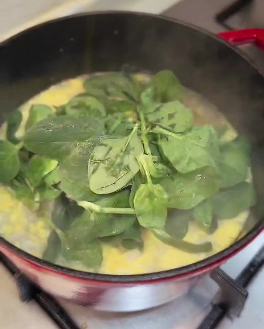 Foglie di spinaci freschi mescolate nella pentola di zuppa pronta.