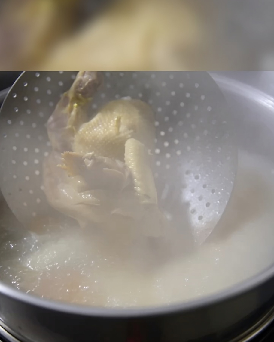 Un pollo intero cotto viene immerso delicatamente in una pentola di brodo di ossa in ebollizione.