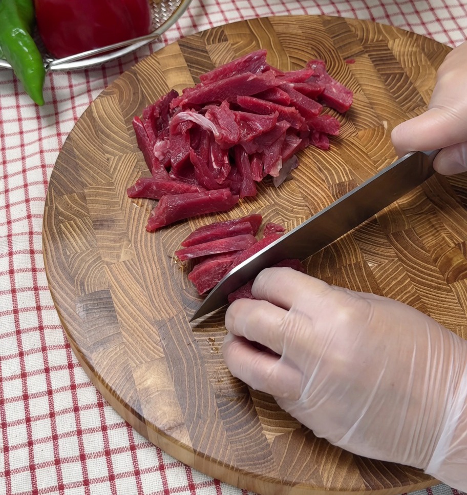Manzo crudo tagliato a striscioline sottili su un tagliere di legno.