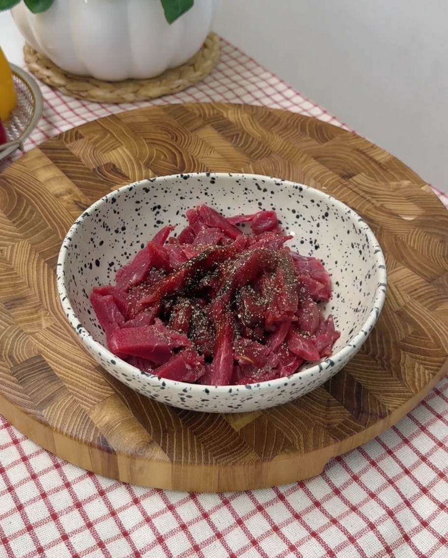 Mano che mescola le strisce di manzo condite in una ciotola.