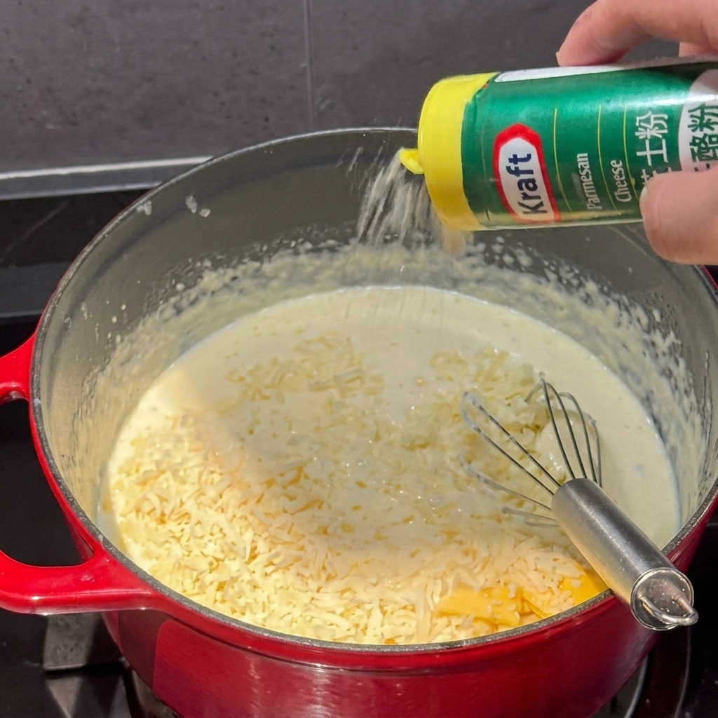 Polvere di formaggio versata da un contenitore nella pentola di salsa cremosa.