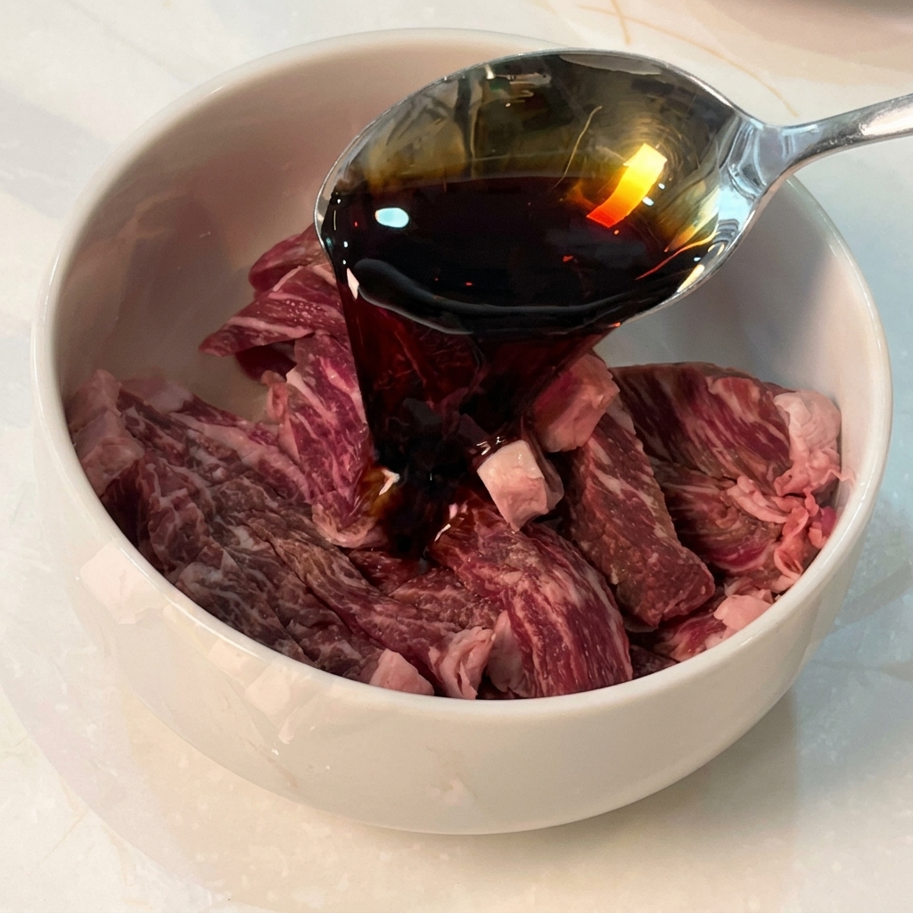 Salsa di soia versata da un cucchiaio in una ciotola con strisce di manzo crudo e altri condimenti.