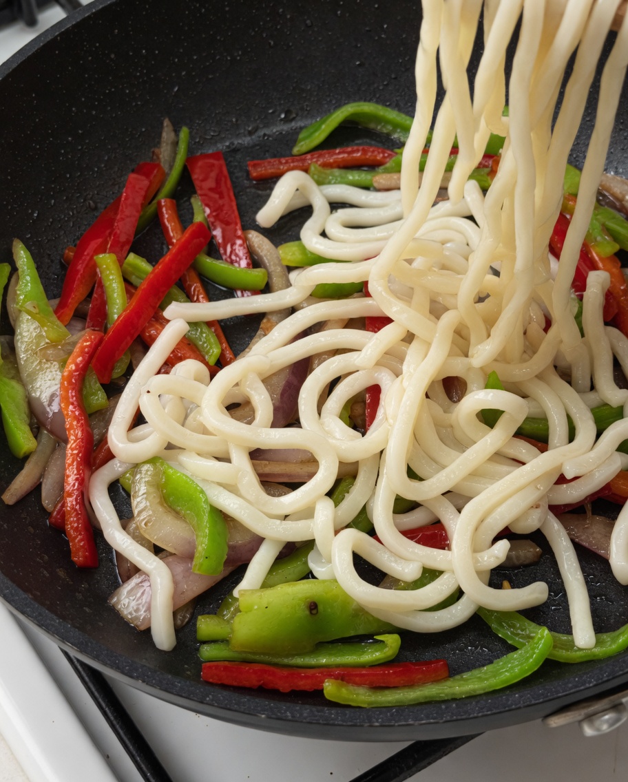 Noodles udon e strisce di manzo aggiunti alla padella con le verdure.
