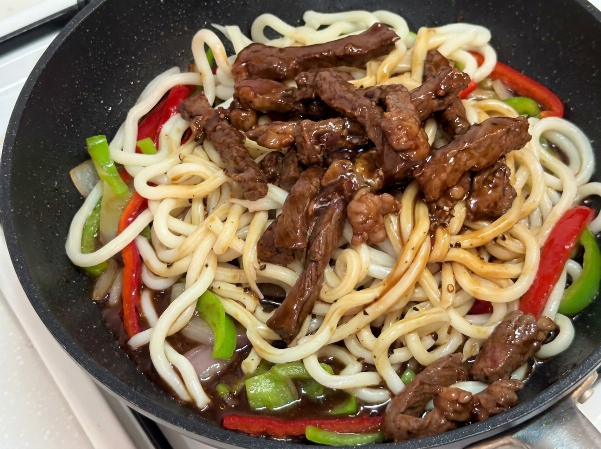 Stir-fry saltato con le pinze nella padella fino a ricoprirlo di salsa.